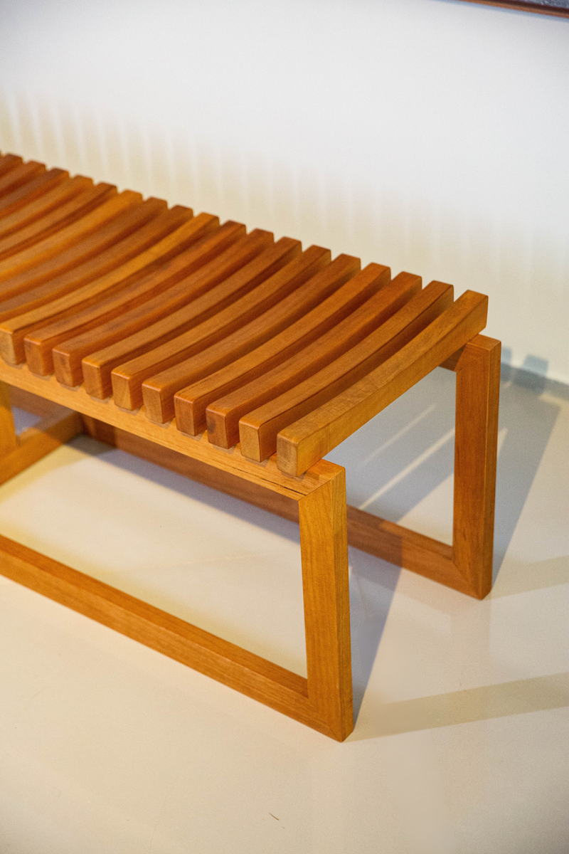 Banco Sucello com estrutura em madeira maciça de Jequitibá, 160 cm de largura, ideal para salas, varandas cobertas e espaços internos. Design minimalista e acabamento na cor Mel, perfeito para diversos estilos de decoração.