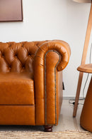 Sofá Chesterfield em couro Amelie caramelo com encosto em capitonê, dimensões de 250 cm de largura, 75 cm de altura e 80 cm de profundidade. Estrutura de madeira tratada, espuma certificada e percintas elásticas italianas. Ideal para ambientes sofisticados. Outros itens na fotografia não estão incluídos.