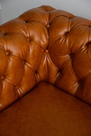 Sofá Chesterfield em couro Amelie caramelo com encosto em capitonê, dimensões de 250 cm de largura, 75 cm de altura e 80 cm de profundidade. Estrutura de madeira tratada, espuma certificada e percintas elásticas italianas. Ideal para ambientes sofisticados. Outros itens na fotografia não estão incluídos.