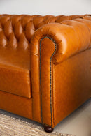 Sofá Chesterfield em couro Amelie caramelo com encosto em capitonê, dimensões de 250 cm de largura, 75 cm de altura e 80 cm de profundidade. Estrutura de madeira tratada, espuma certificada e percintas elásticas italianas. Ideal para ambientes sofisticados. Outros itens na fotografia não estão incluídos.