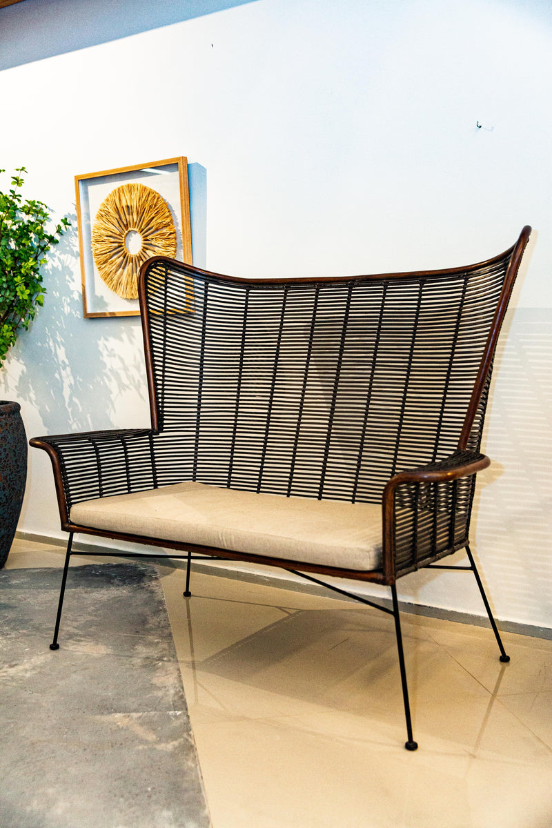 Sofá Manila feito à mão com estrutura em rattan natural, projetado para duas pessoas. Dimensões: 100 cm (A) x 120 cm (L) x 80 cm (P). Ideal para salas de estar, varandas ou áreas externas cobertas. Produto artesanal com variações de cor e textura. Outros itens na fotografia não estão incluídos.