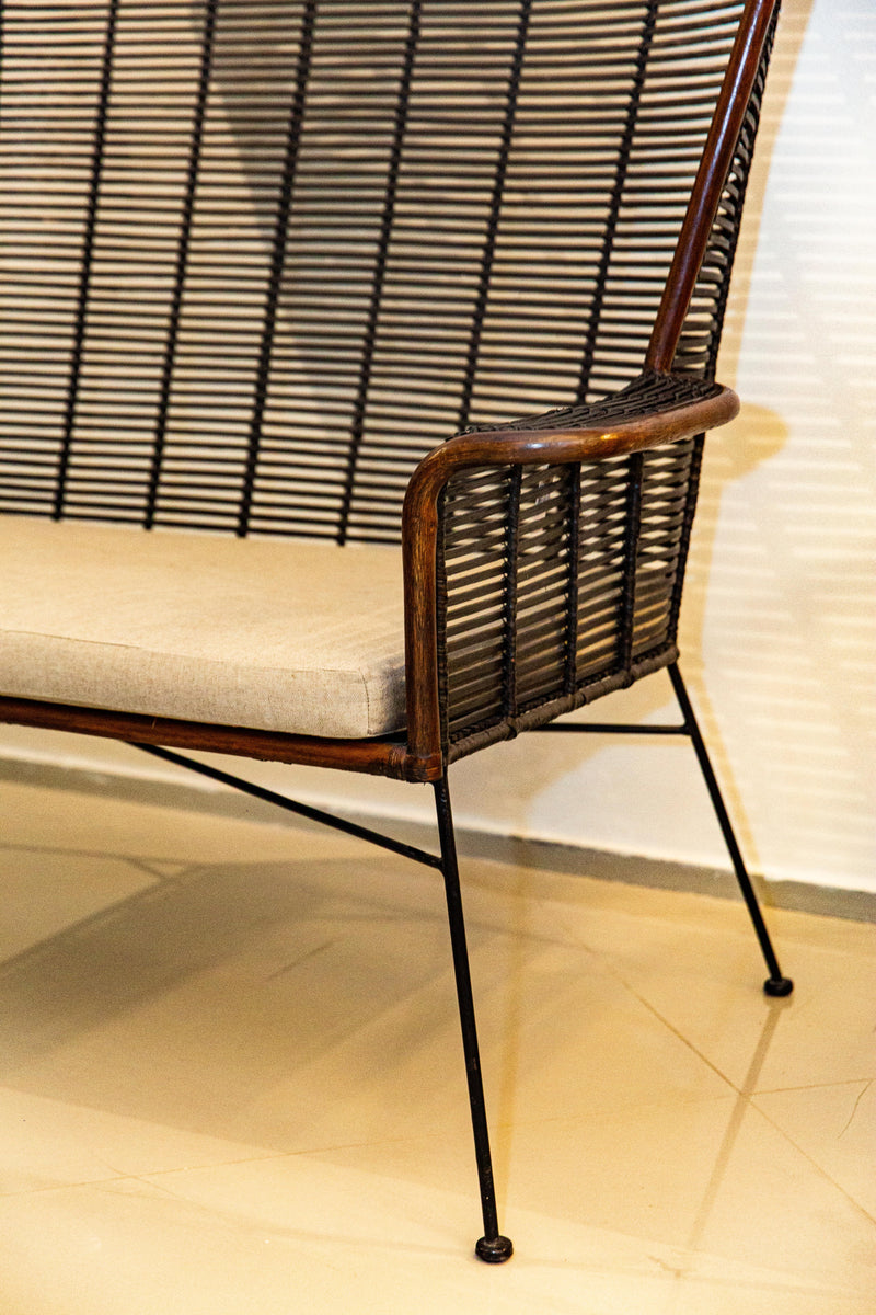 Sofá Manila feito à mão com estrutura em rattan natural, projetado para duas pessoas. Dimensões: 100 cm (A) x 120 cm (L) x 80 cm (P). Ideal para salas de estar, varandas ou áreas externas cobertas. Produto artesanal com variações de cor e textura. Outros itens na fotografia não estão incluídos.