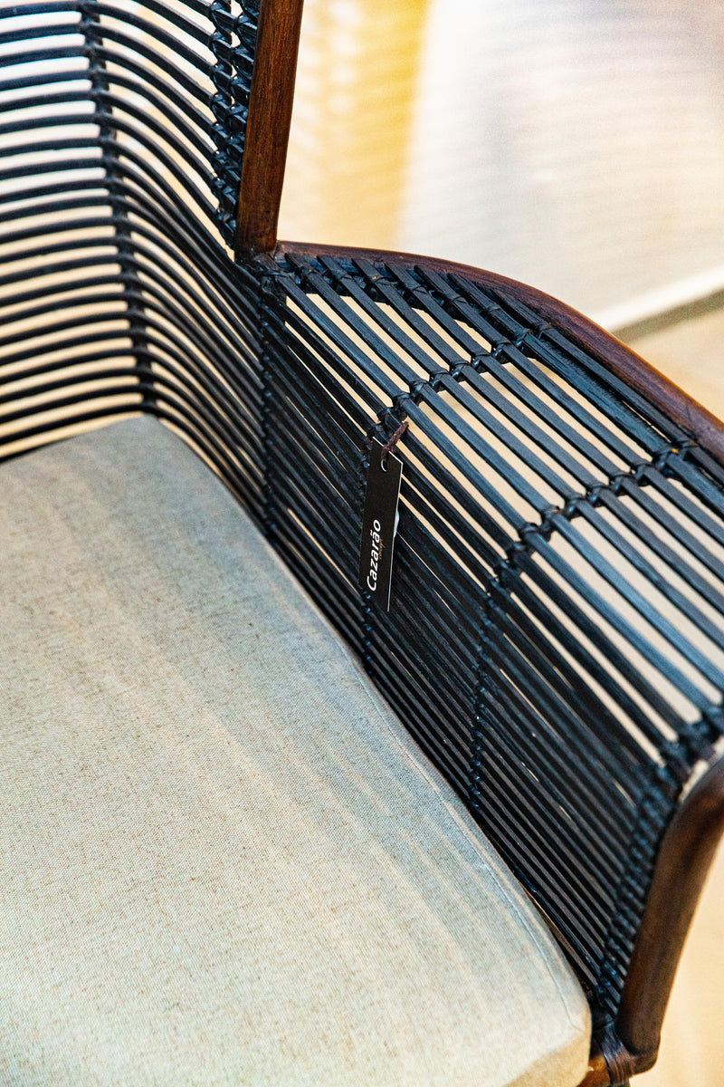 Sofá Manila feito à mão com estrutura em rattan natural, projetado para duas pessoas. Dimensões: 100 cm (A) x 120 cm (L) x 80 cm (P). Ideal para salas de estar, varandas ou áreas externas cobertas. Produto artesanal com variações de cor e textura. Outros itens na fotografia não estão incluídos.